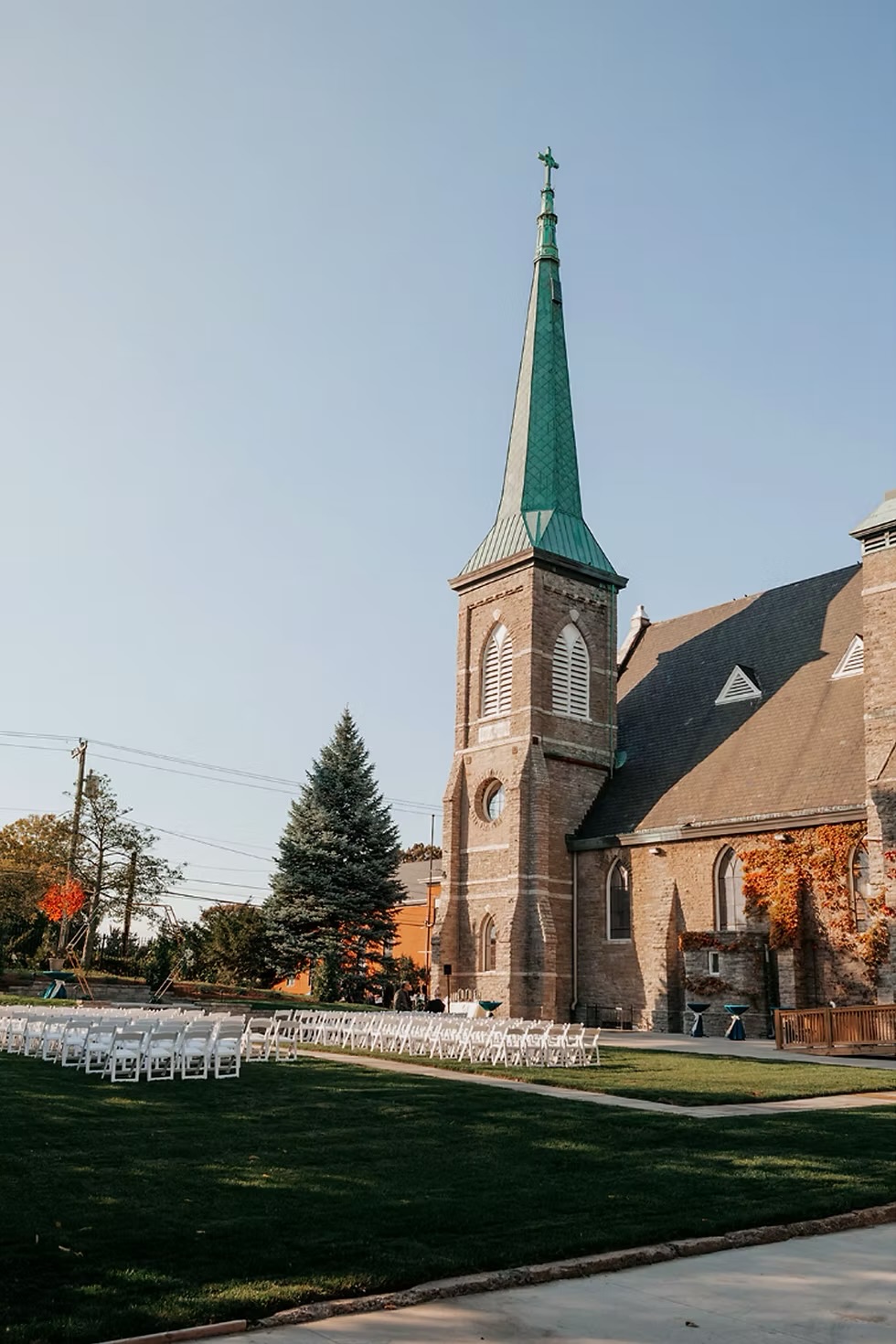 Rows of white chairs set for a ceremony on the lawn at
                          The Palomar, with the stone church and its green
                          steeple behind them and autumn leaves on the walls.